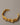 A close-up of a chunky, premium open-cuff bracelet featuring an irregular molten gold and crushed foil texture, made of real gold-plated brass, resting elegantly on a smooth grey background.-1
