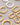 A pair of highly polished, minimalist thick tubular hoop earrings electroplated in 18K real gold, featuring a secure snap closure, resting on a white decorative stone against a grey background.-2