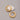 A pair of highly polished, minimalist thick tubular hoop earrings electroplated in 18K real gold, featuring a secure snap closure, resting on a white decorative stone against a grey background.-1