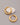 A pair of highly polished, minimalist thick tubular hoop earrings electroplated in 18K real gold, featuring a secure snap closure, resting on a white decorative stone against a grey background.-1